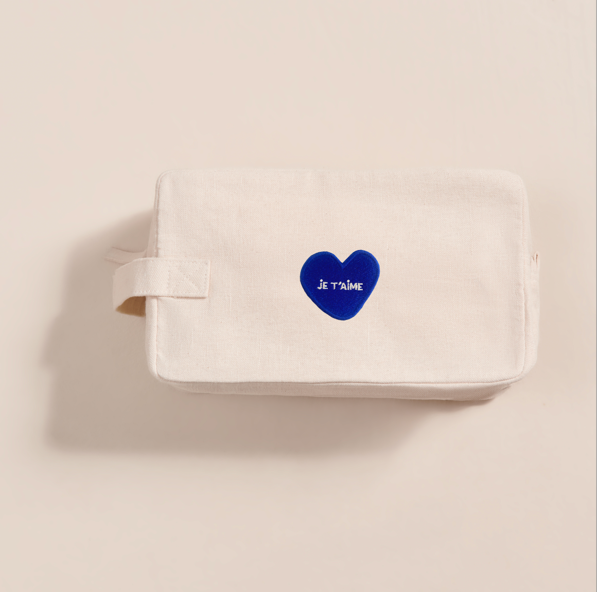 La trousse de toilette émoi émoi est décoré d'un coeur bleu brodé sur lequel est écrit Je t'aime